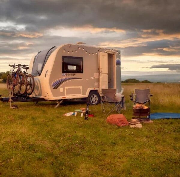 Bailey Discovery caravan in a green field with camping chairs and a fire set up