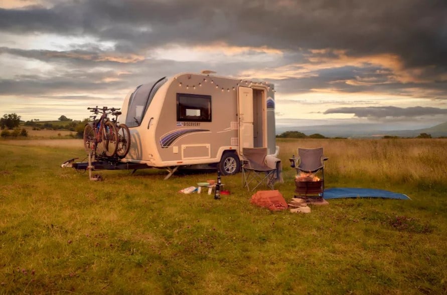 Bailey Discovery caravan in a green field with camping chairs and a fire set up