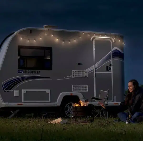 Two people sitting outside a Bailey Discovery at night time with a fire pit and fairy lights