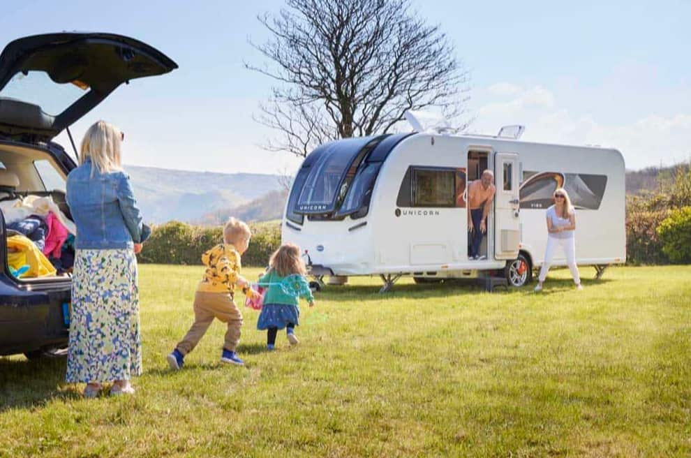 bailey uniron series 5 caravan in a green field with a blue sky and family members surrounding the caravan